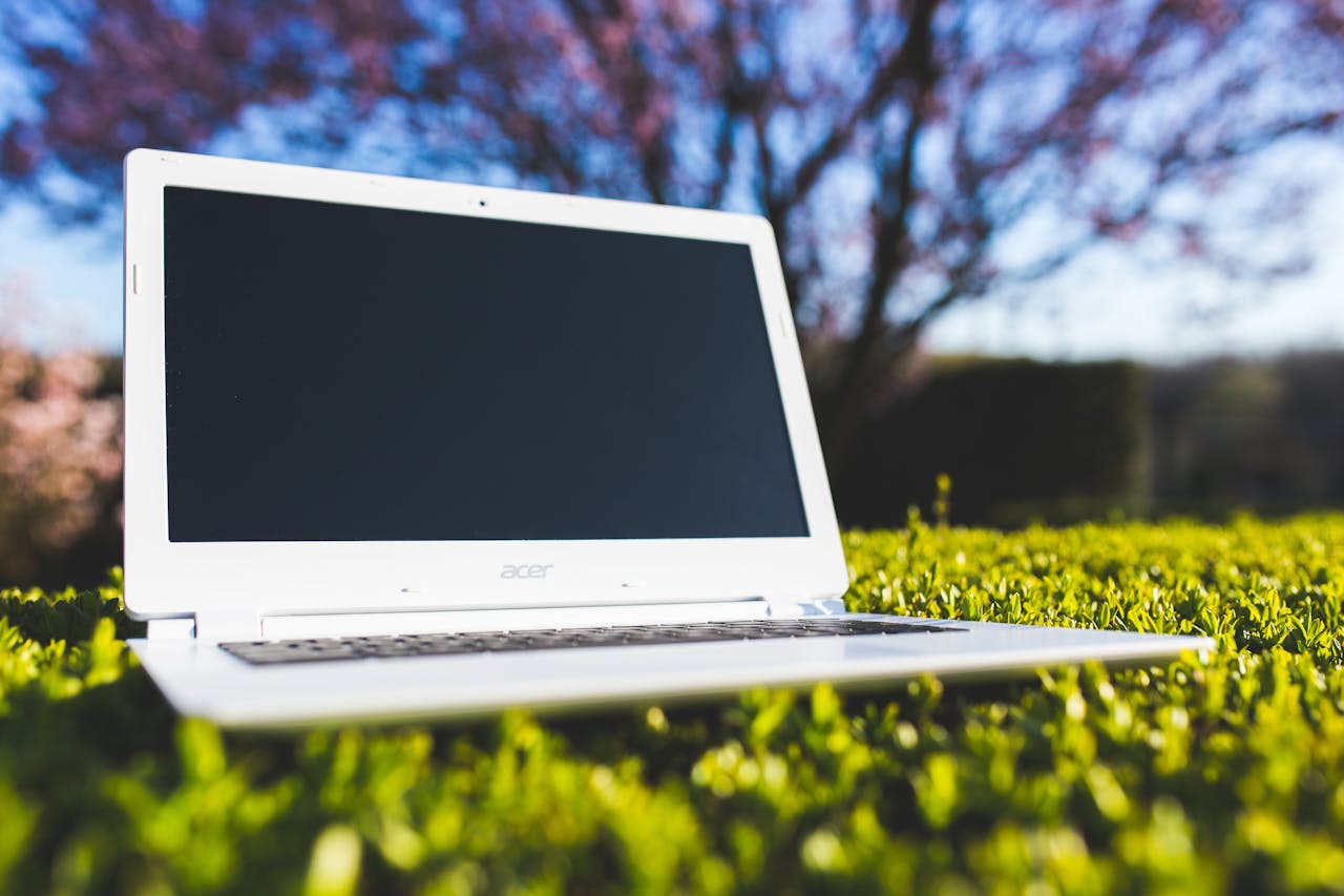 about-img White laptop on green grass in a spring garden with a blossoming tree in the background.